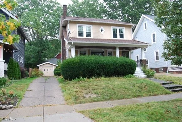 View of front of house featuring covered porch, an outbuilding, a chimney, a garage, and a front lawn