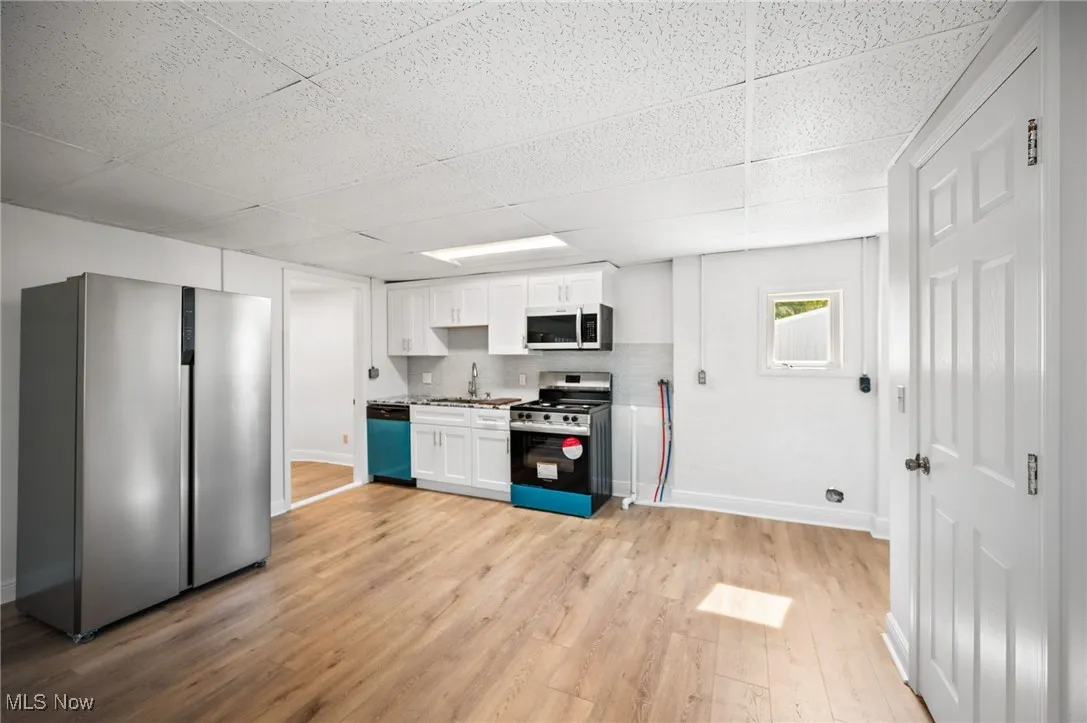 Kitchen featuring stainless steel appliances, white cabinets, vinyl flooring, a paneled ceiling, and tasteful backsplash