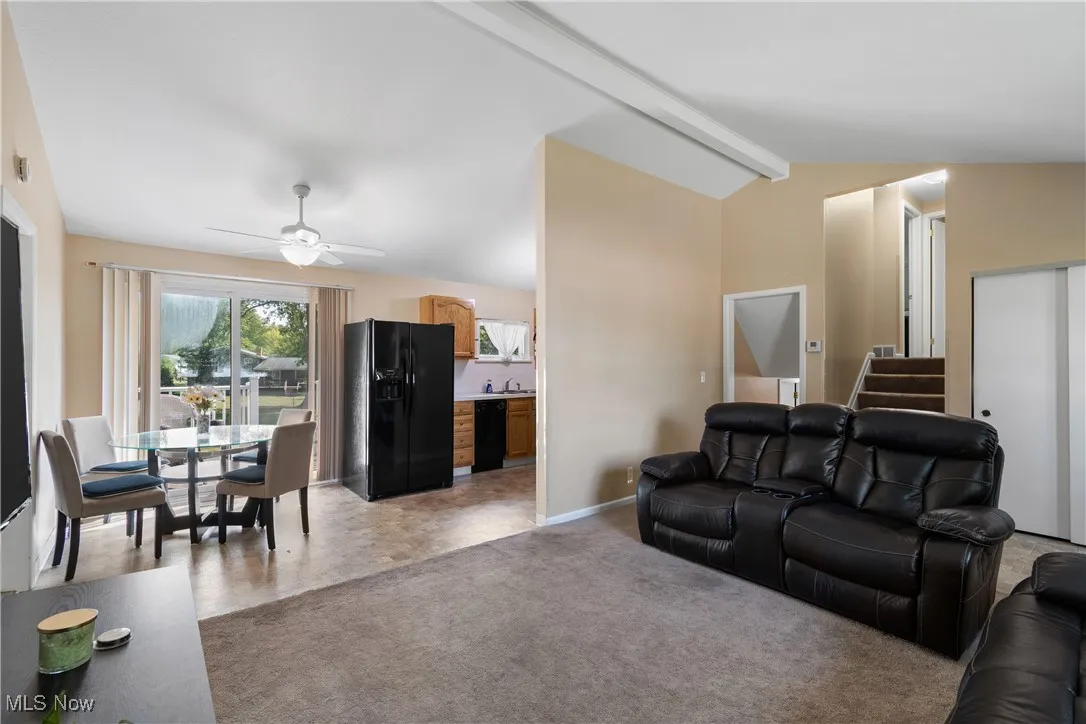 Living area with a ceiling fan, light colored carpet, and stairs