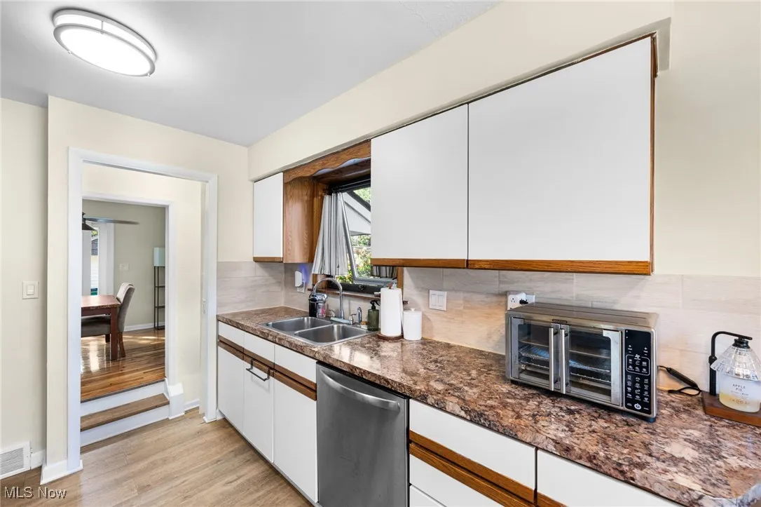 Kitchen with white cabinetry, tasteful backsplash, light wood-style flooring, dishwasher, and brown cabinetry