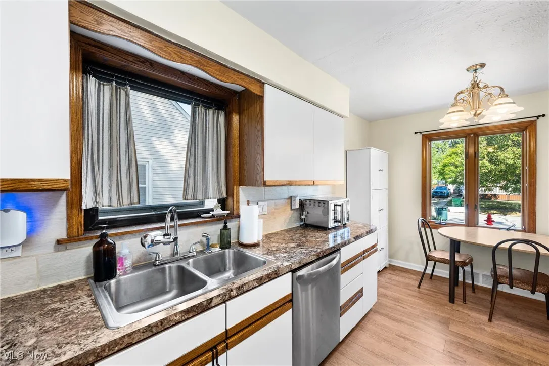 Kitchen with dark countertops, white cabinets, light wood-style flooring, dishwasher, and pendant lighting