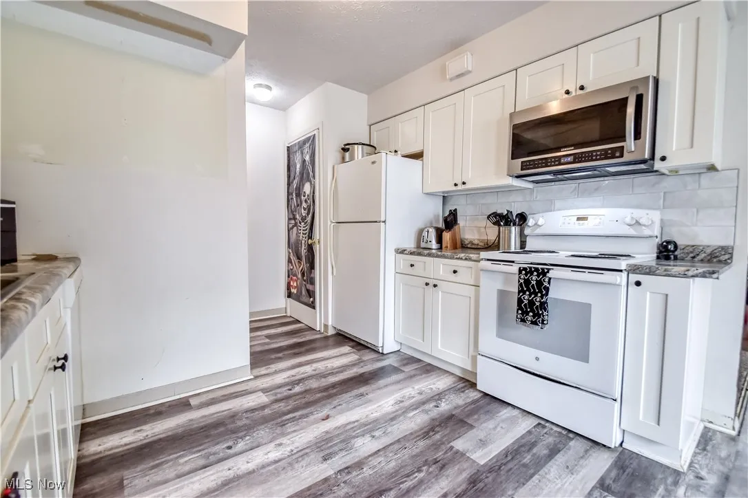 Kitchen with white appliances, white cabinetry, backsplash, light wood-type flooring, and a textured ceiling