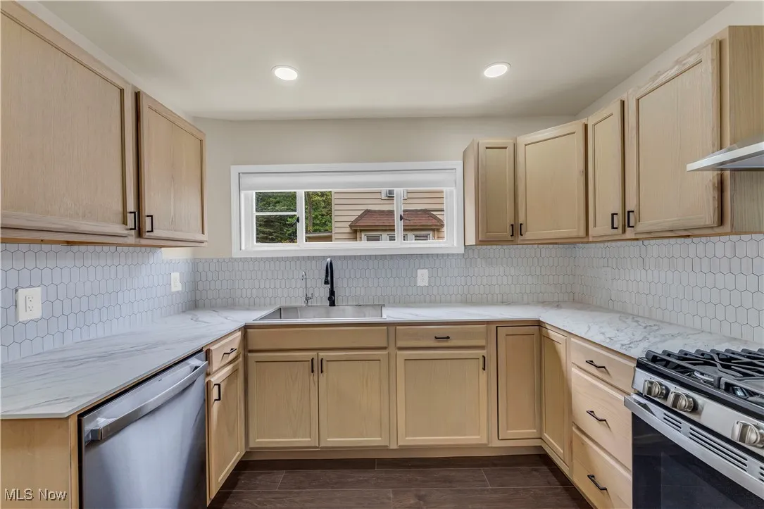 Kitchen with light brown cabinets, tasteful backsplash, appliances with stainless steel finishes, light stone counters, and recessed lighting