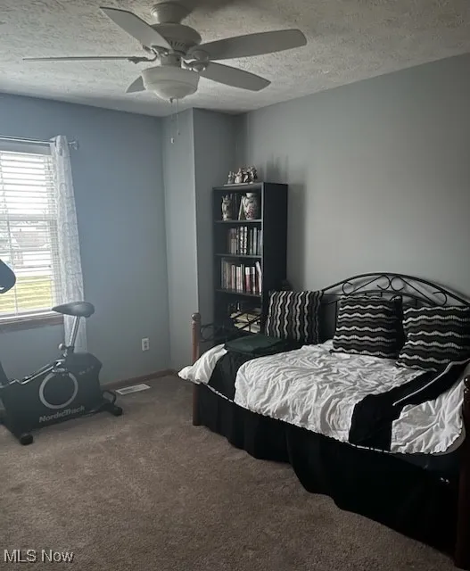 Bedroom with a textured ceiling, carpet flooring, and ceiling fan