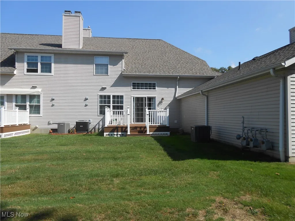 Rear view of house featuring a wooden deck, a chimney, a lawn, and a shingled roof
