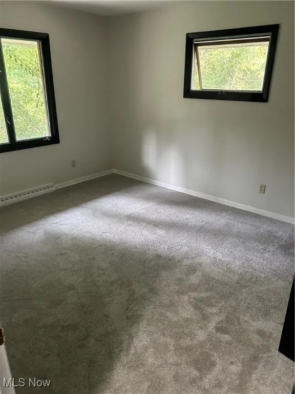Carpeted spare room with baseboard heating and baseboards