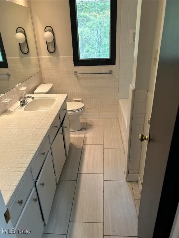 Full bathroom with tile walls, a wainscoted wall, vanity, and light tile patterned flooring