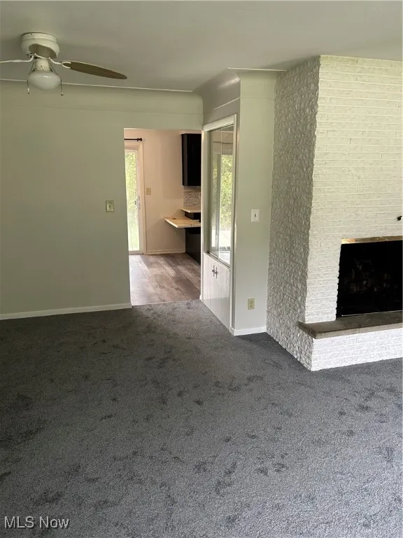 Unfurnished living room featuring a fireplace, a ceiling fan, plenty of natural light, and dark carpet