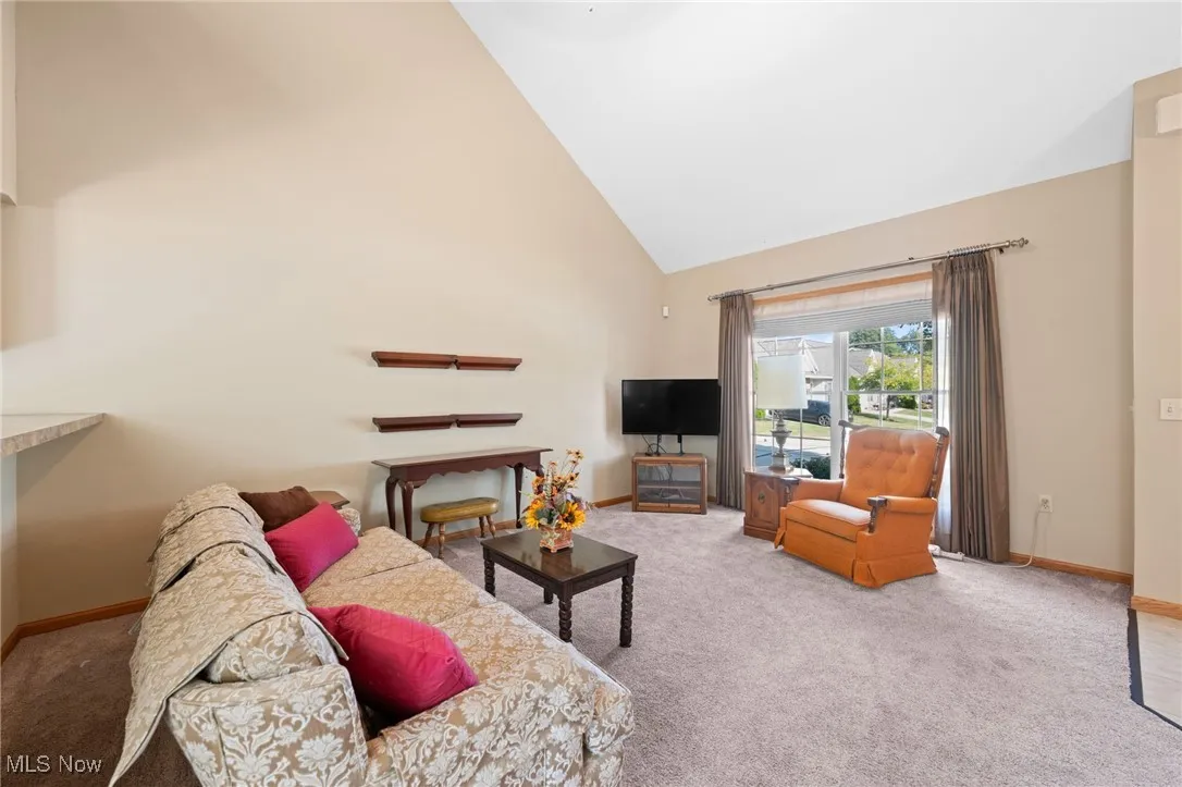 Carpeted living room with high vaulted ceiling and baseboards