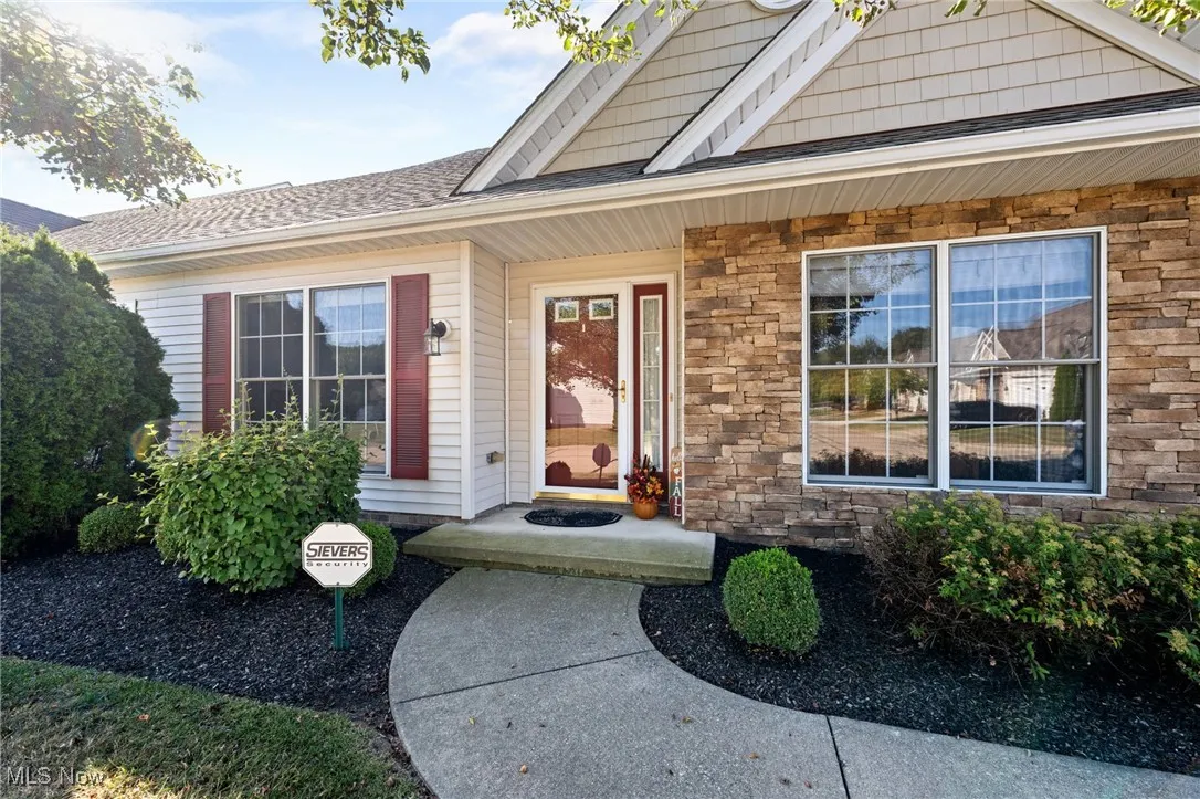 Entrance to property featuring stone siding, covered porch, and roof with shingles