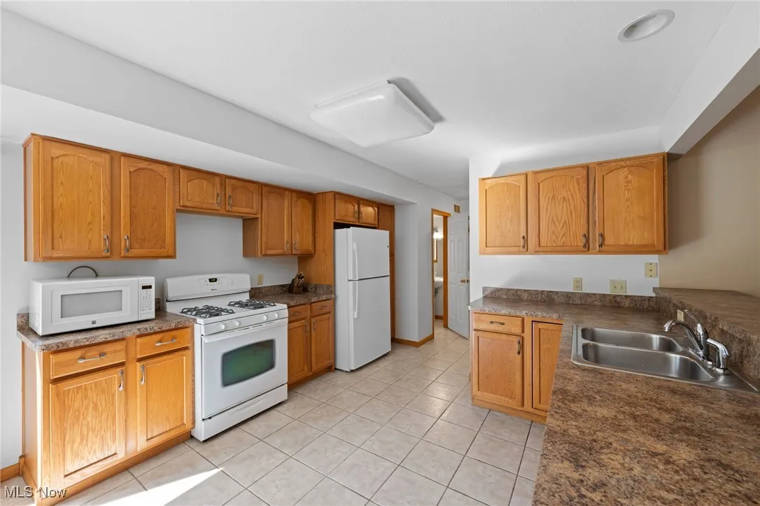 Kitchen featuring white appliances, light tile patterned floors, dark countertops, and brown cabinets