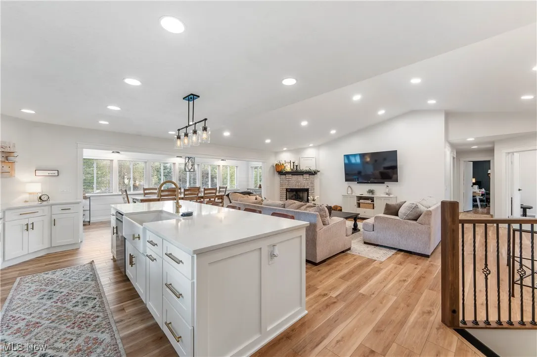 Kitchen with white cabinetry, hanging light fixtures, a fireplace, an island with sink, and vaulted ceiling
