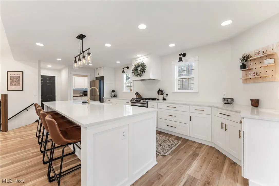 Kitchen with white cabinetry, decorative light fixtures, a breakfast bar, a center island with sink, and recessed lighting