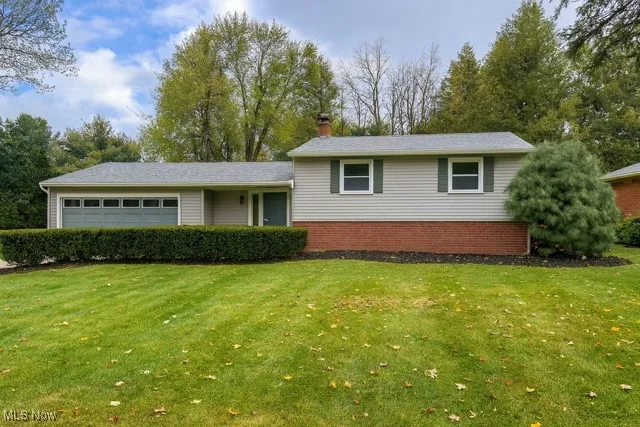 Tri-level home with a chimney, brick siding, a front lawn, and a garage