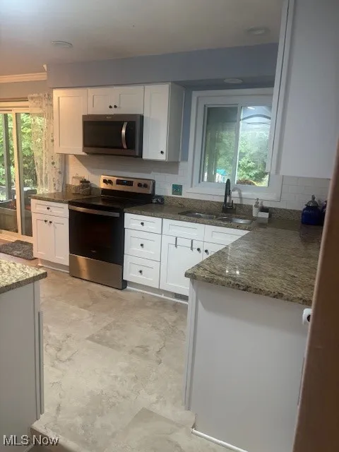 Kitchen with stainless steel range oven, white cabinets, dark stone counters, and crown molding