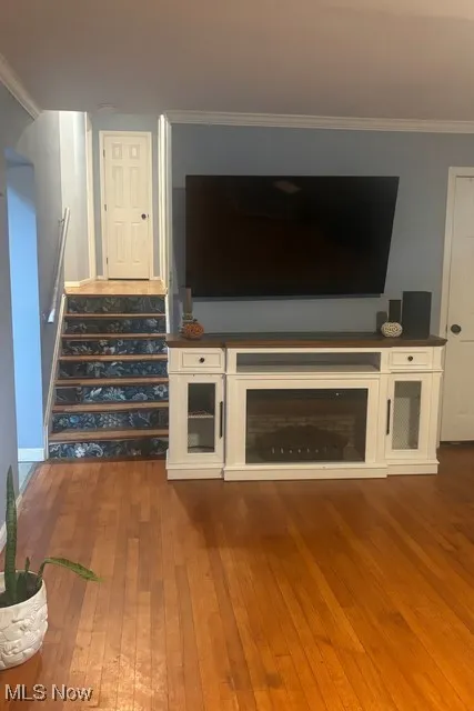 Unfurnished living room featuring dark wood-type flooring, stairs, and crown molding