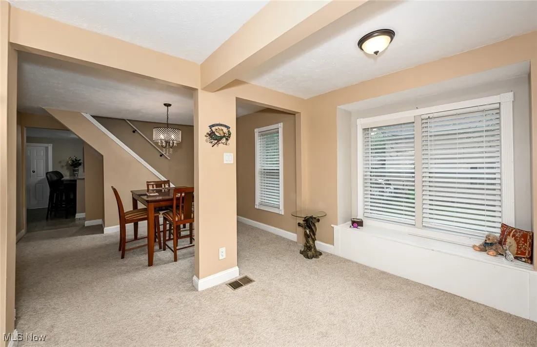 Carpeted dining space with beamed ceiling and a chandelier