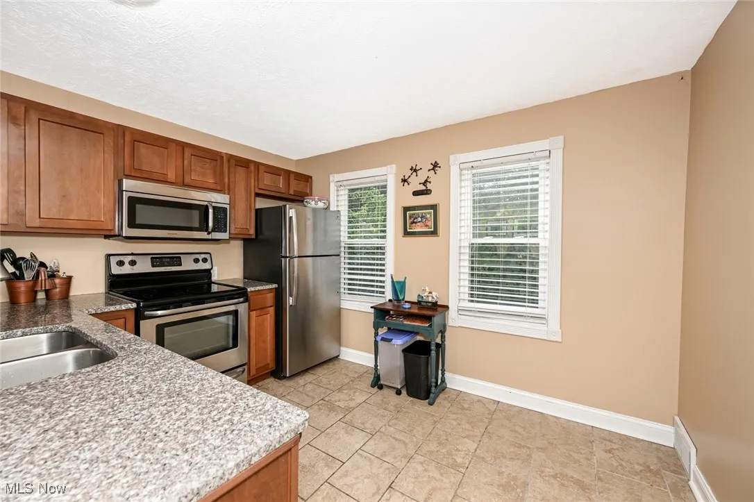 Kitchen featuring stainless steel appliances, brown cabinetry, light stone counters, light tile patterned floors, and a textured ceiling