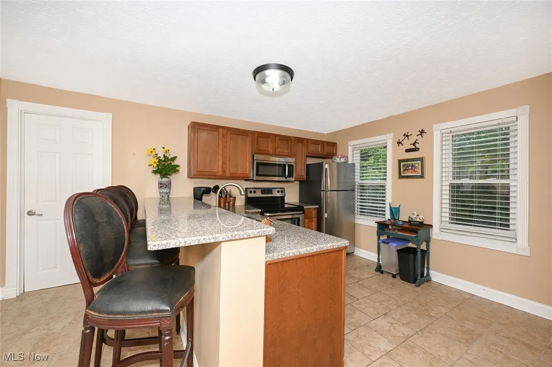 Kitchen featuring brown cabinets, a breakfast bar, stainless steel appliances, a peninsula, and light stone counters
