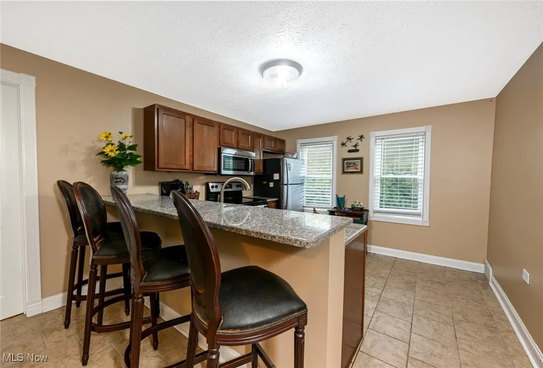Kitchen with a peninsula, light stone counters, a kitchen bar, a textured ceiling, and appliances with stainless steel finishes