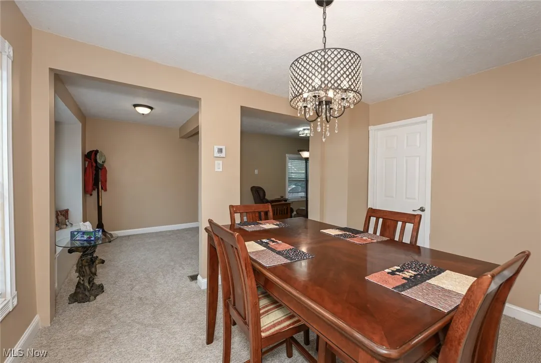 Dining area featuring light colored carpet, a chandelier, and a textured ceiling