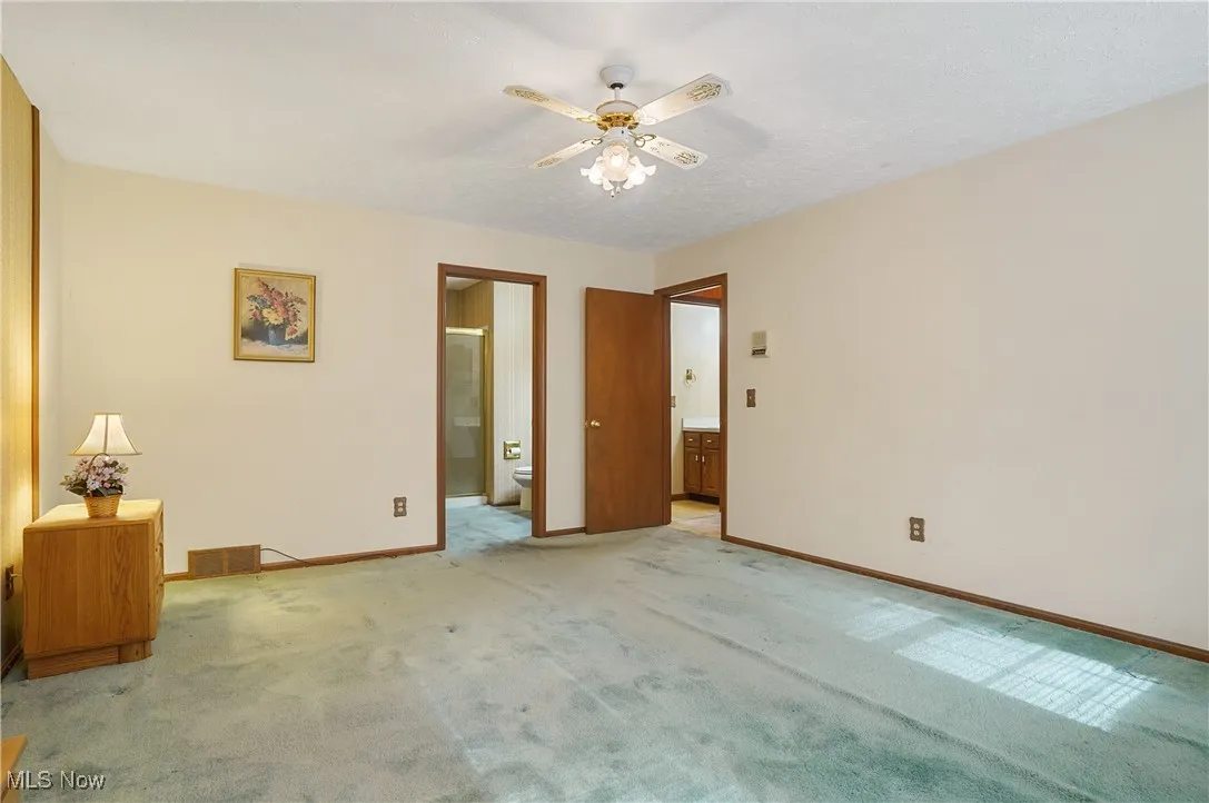 Unfurnished bedroom with ensuite bathroom, carpet, and a ceiling fan