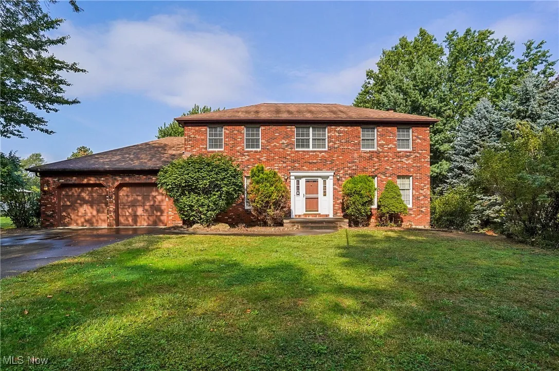 Colonial house with brick siding, a front yard, asphalt driveway, and an attached garage