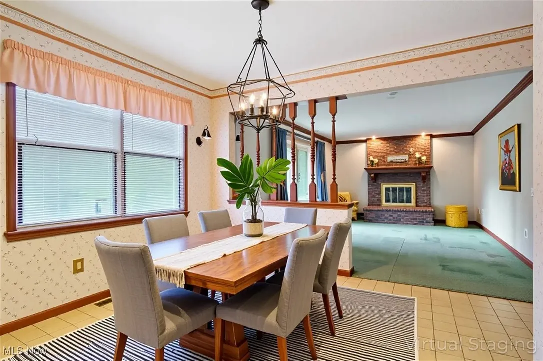 Dining room with wallpapered walls, light tile patterned flooring, a brick fireplace, ornamental molding, and a chandelier