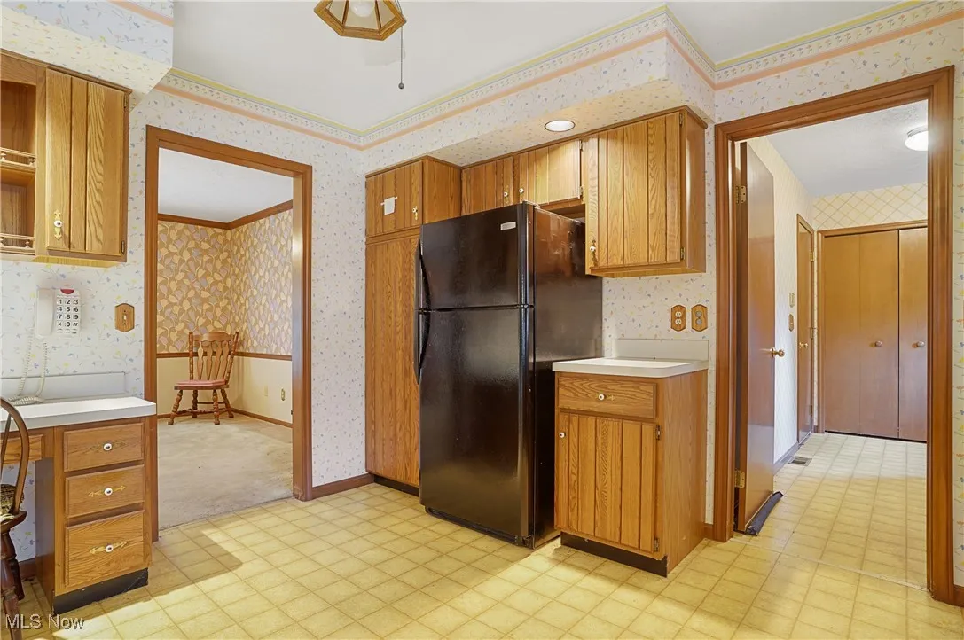 Kitchen featuring light floors, wallpapered walls, freestanding refrigerator, light countertops, and brown cabinets