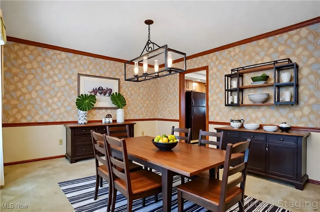 Dining space with wallpapered walls, ornamental molding, light colored carpet, and a chandelier