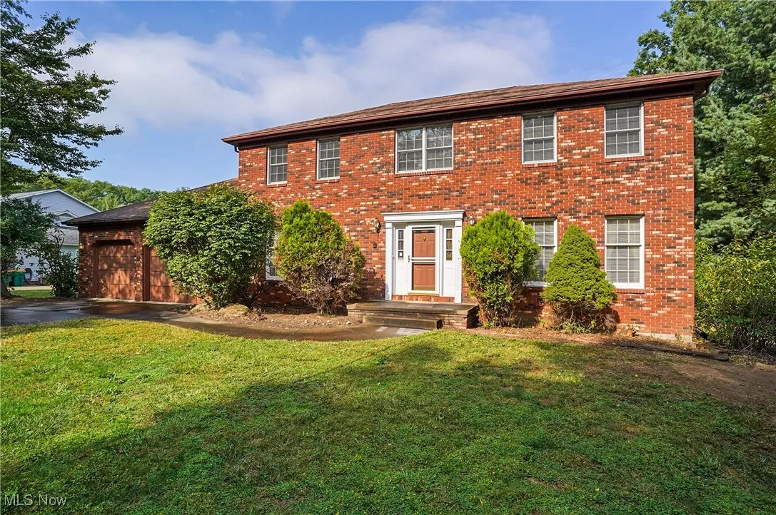 Colonial-style house with brick siding, a front lawn, and asphalt driveway