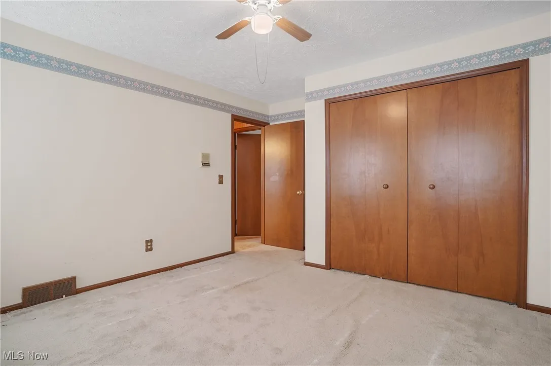 Unfurnished bedroom with a textured ceiling, light colored carpet, a ceiling fan, and a closet