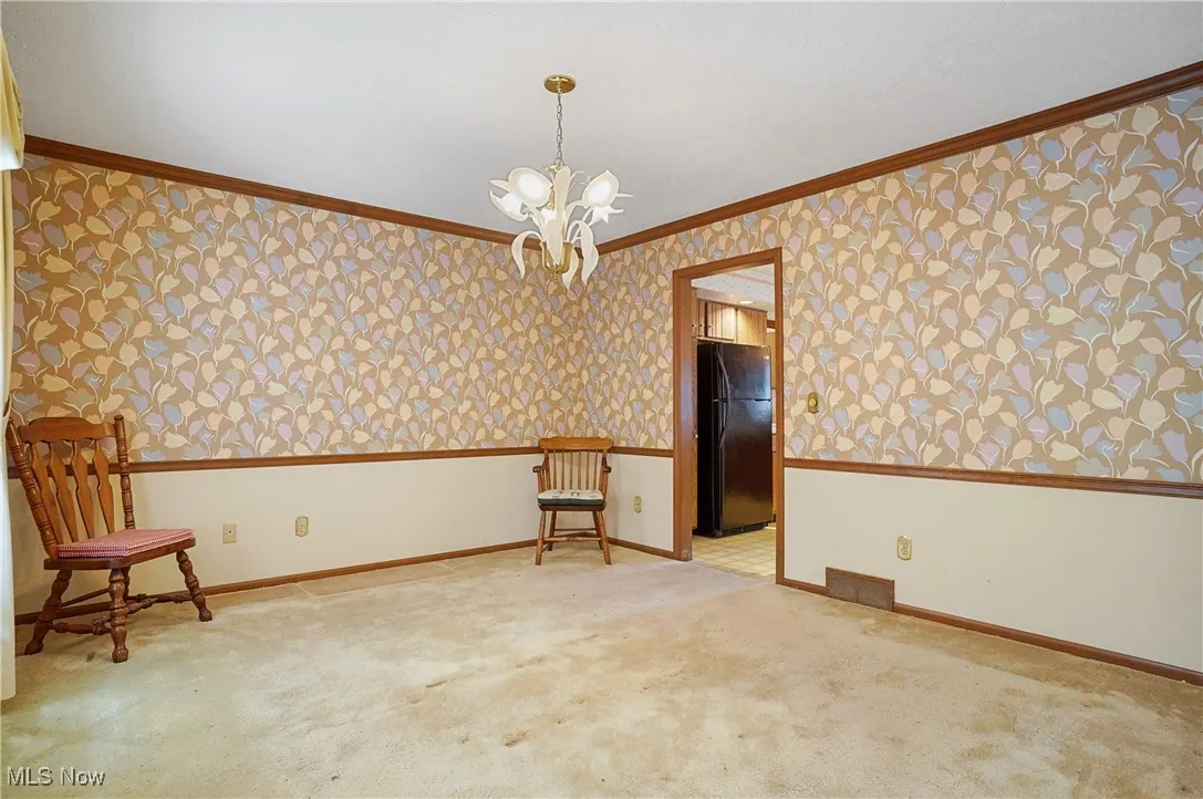 Spare room with wallpapered walls, ornamental molding, a chandelier, and carpet floors
