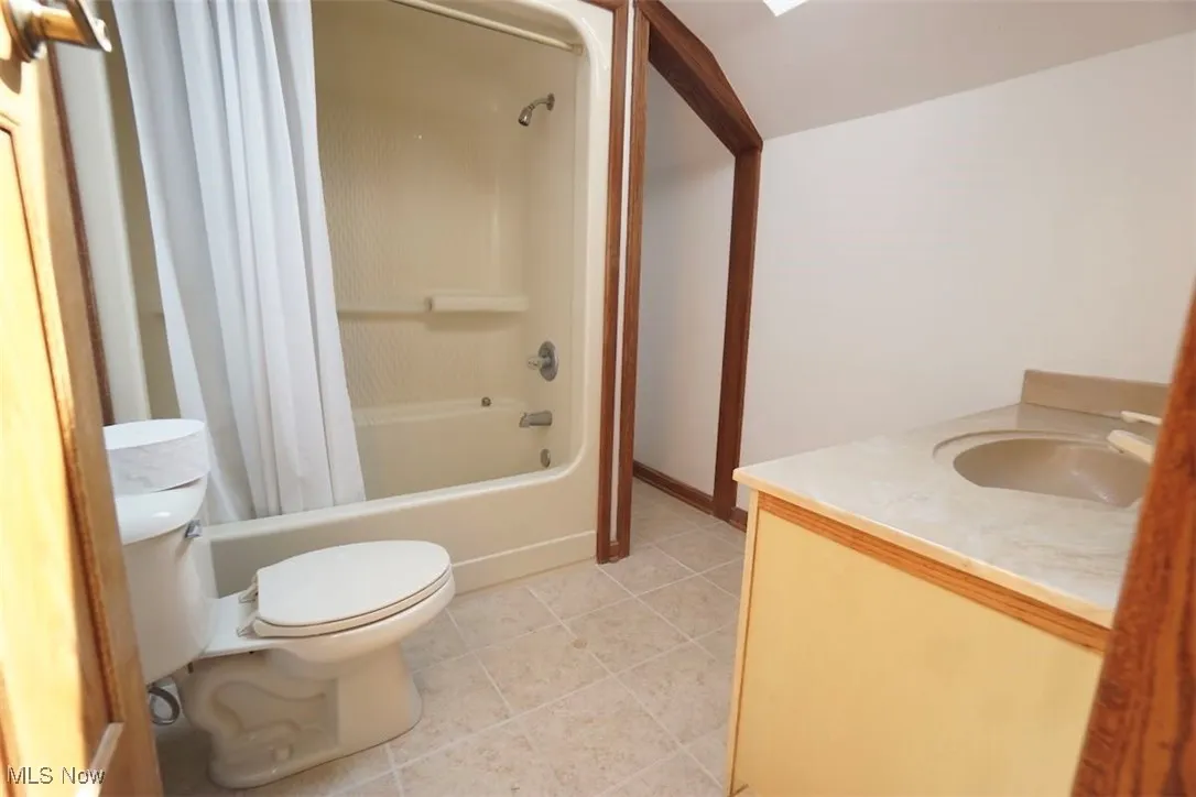 Full bathroom with shower / tub combo with curtain, vanity, light tile patterned flooring, lofted ceiling, and a skylight