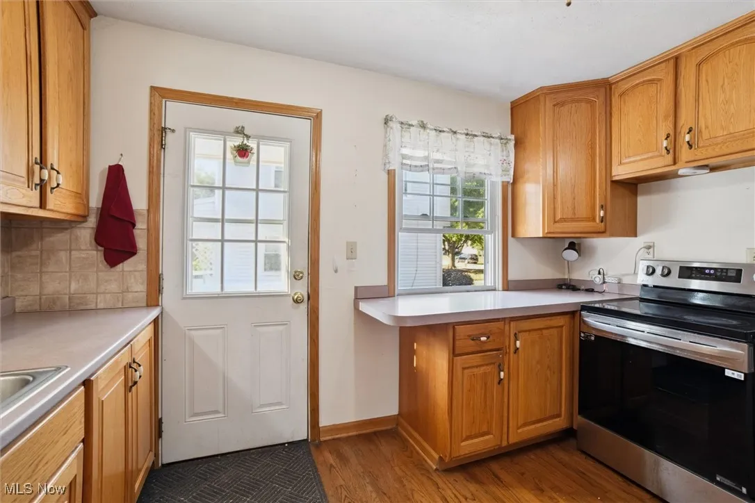 Kitchen with stainless steel range with electric stovetop, brown cabinets, light countertops, dark wood-type flooring, and backsplash