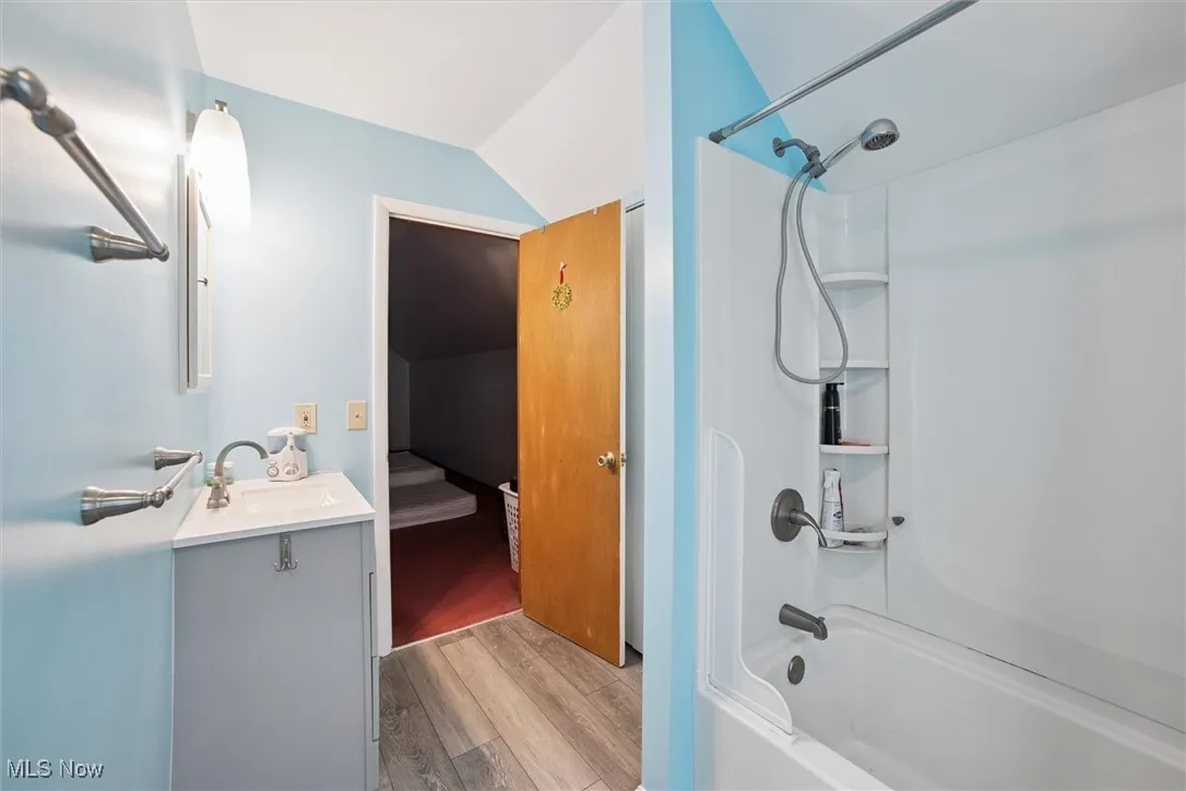 Bathroom with washtub / shower combination, light wood-type flooring, vanity, vaulted ceiling, and ensuite bathroom