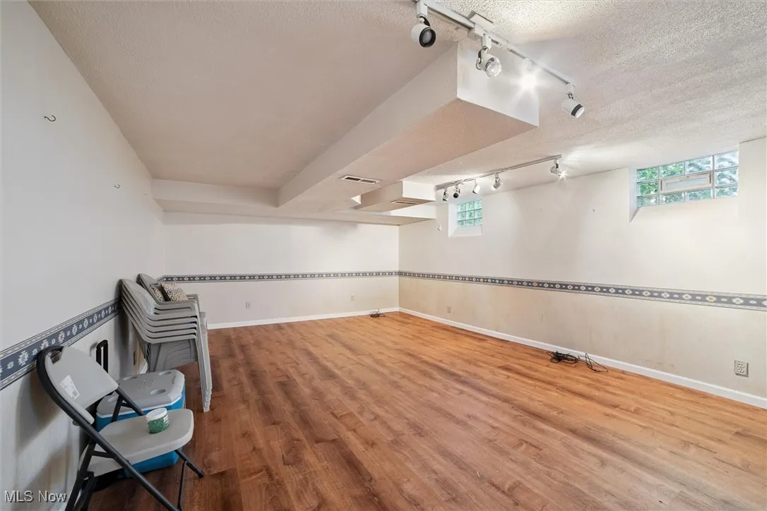 Below grade area with track lighting, a textured ceiling, light wood-style floors, and plenty of natural light