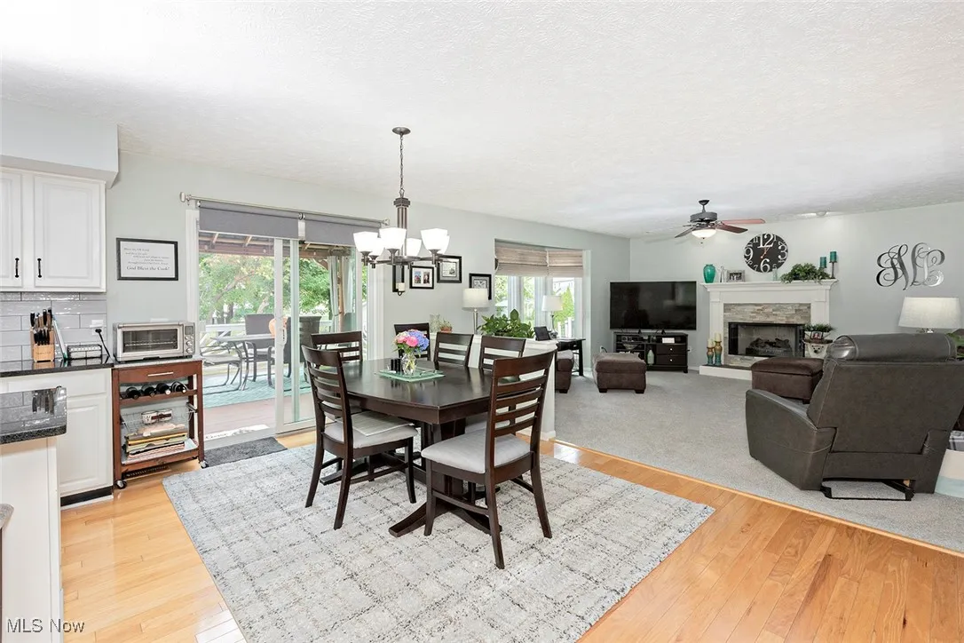Dining area featuring a fireplace, light wood finished floors, ceiling fan, a chandelier, and a textured ceiling