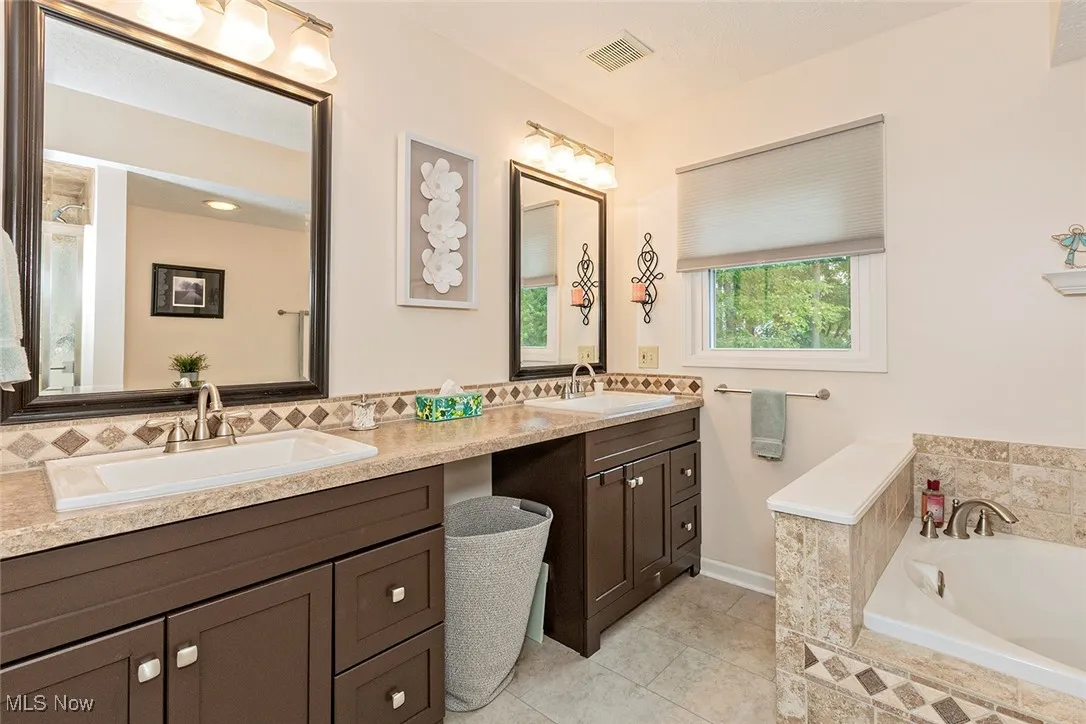 Bathroom featuring double vanity, a bath, light tile patterned floors, and backsplash