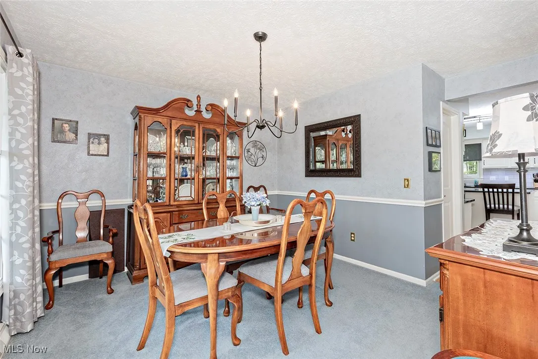 Dining space featuring a chandelier, a textured ceiling, light carpet, and a textured wall