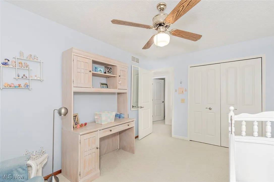 Bedroom featuring built in study area, light colored carpet, ceiling fan, a closet, and a textured ceiling