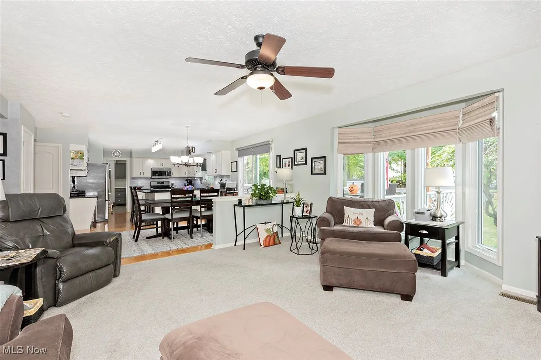 Living area featuring light colored carpet, a textured ceiling, ceiling fan, and a chandelier