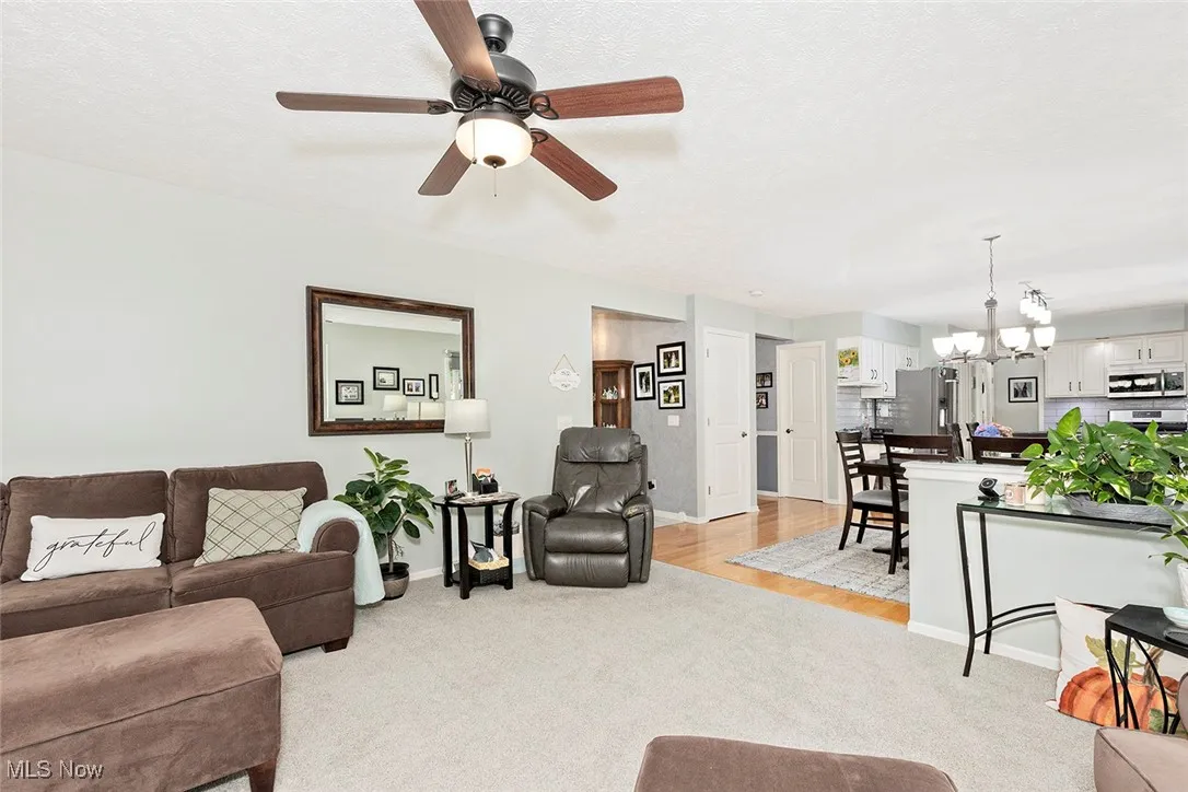 Living room featuring a chandelier, light carpet, a textured ceiling, and ceiling fan