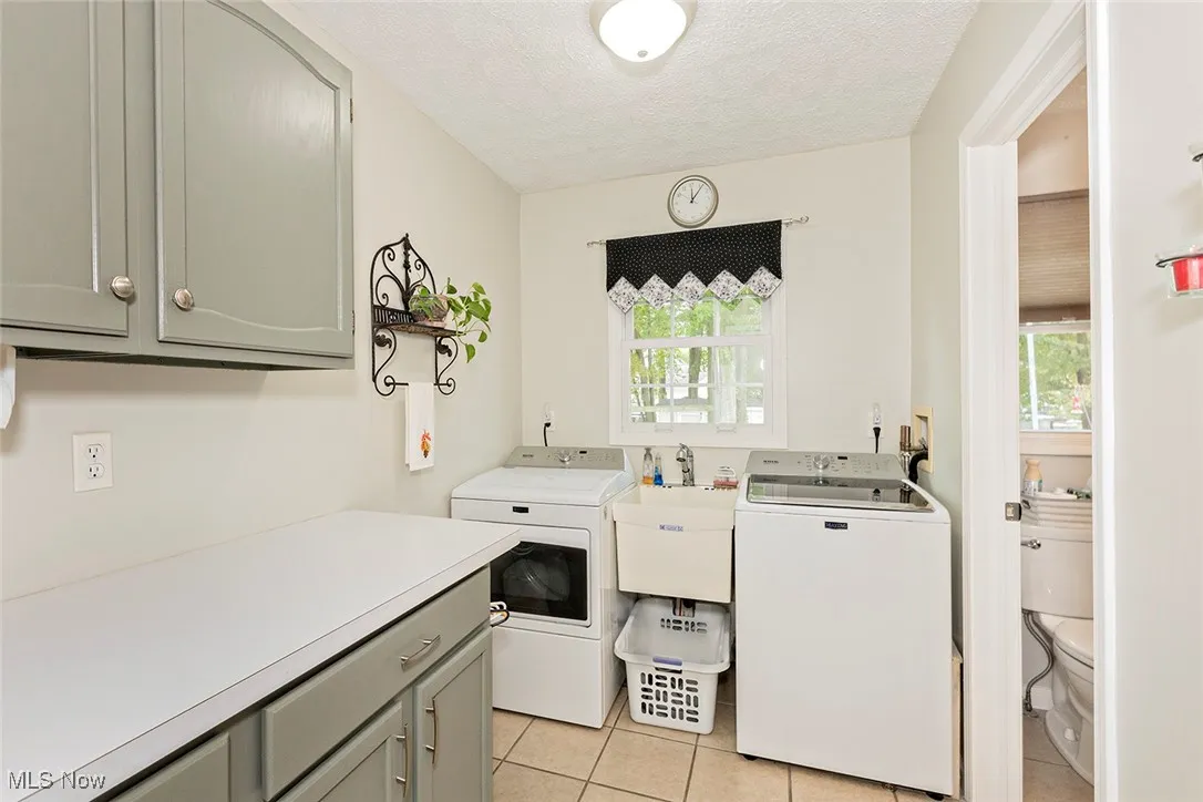 Washroom featuring a textured ceiling, light tile patterned floors, washer and dryer, and cabinet space