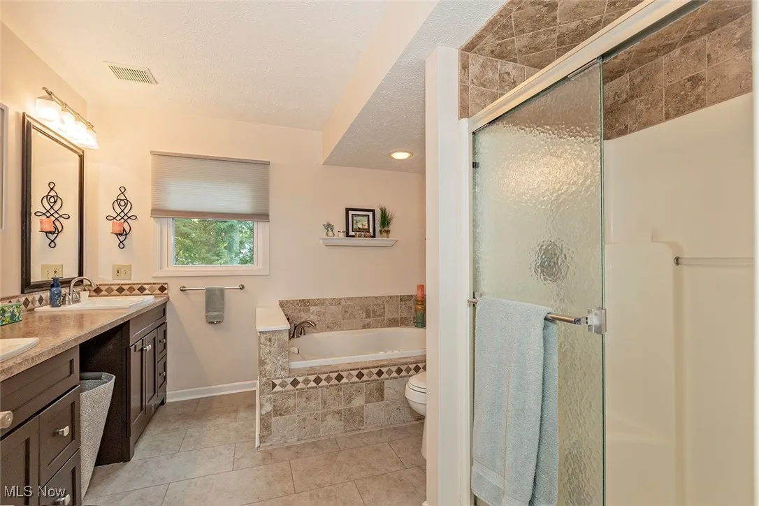 Full bathroom with double vanity, a stall shower, a bath, light tile patterned floors, and a textured ceiling