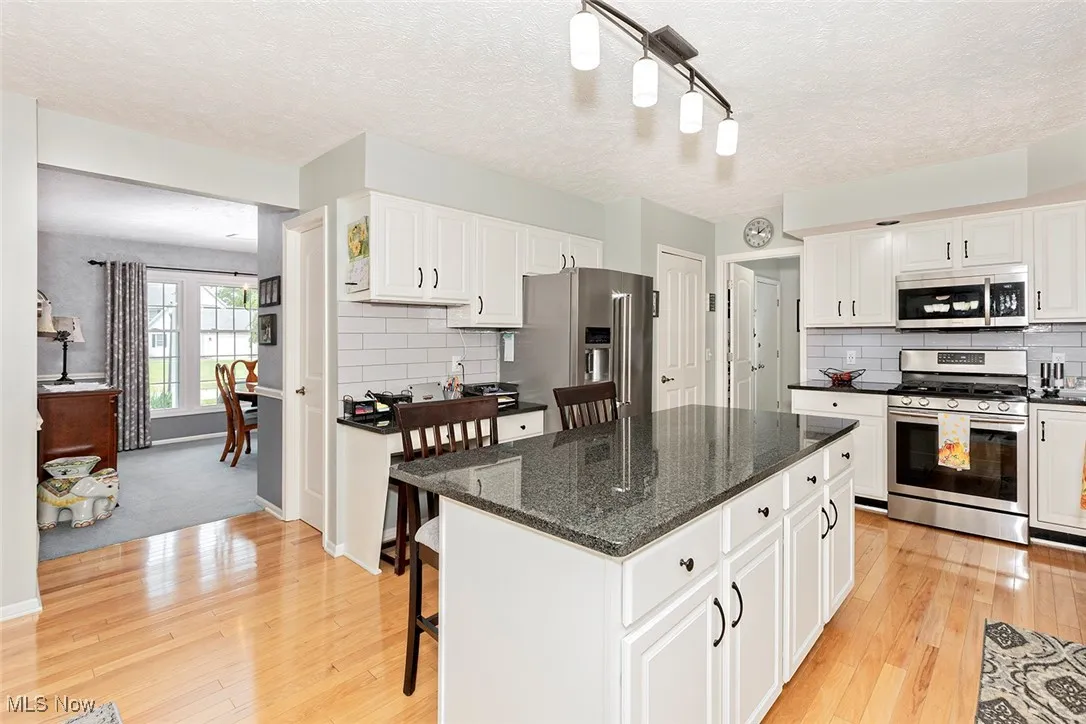 Kitchen with a breakfast bar, appliances with stainless steel finishes, a textured ceiling, dark stone counters, and white cabinetry