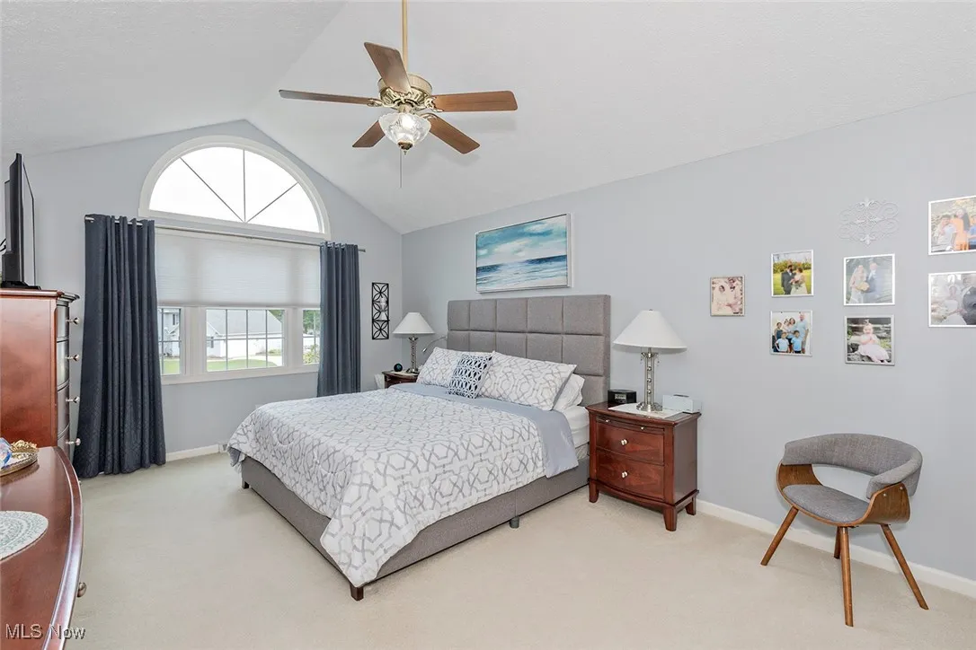 Carpeted bedroom with a ceiling fan and high vaulted ceiling