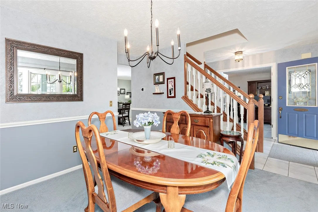 Tiled dining space with a textured ceiling, a chandelier, stairs, and carpet floors