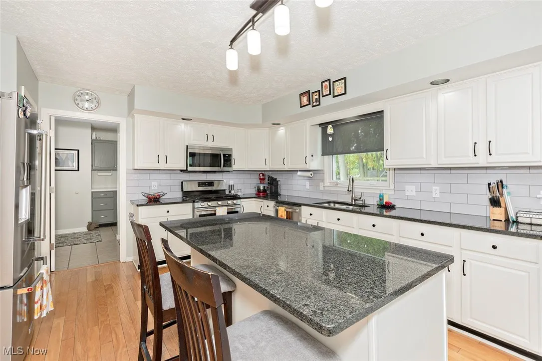 Kitchen with light wood-type flooring, a textured ceiling, appliances with stainless steel finishes, dark stone countertops, and white cabinetry