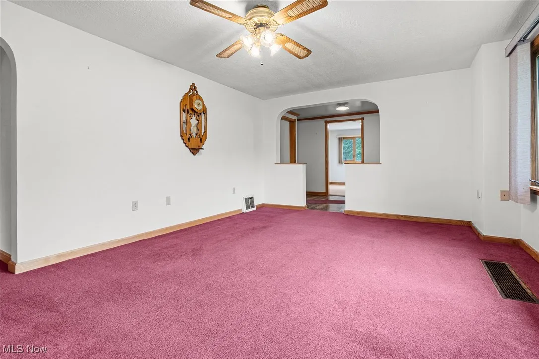 Carpeted empty room featuring arched walkways and ceiling fan